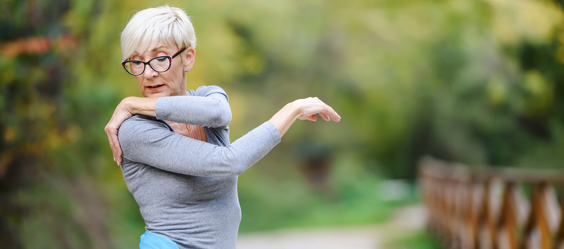 Elderly woman exercising outdoors in nature having shoulder pain